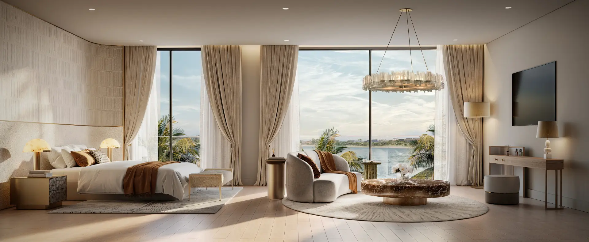 Bedroom at Yas Riva with a bed dressed in white and rust-toned linens, a curved lounge sofa and round marble coffee table, crystal chandelier, and floor-to-ceiling windows overlooking the waterfront.