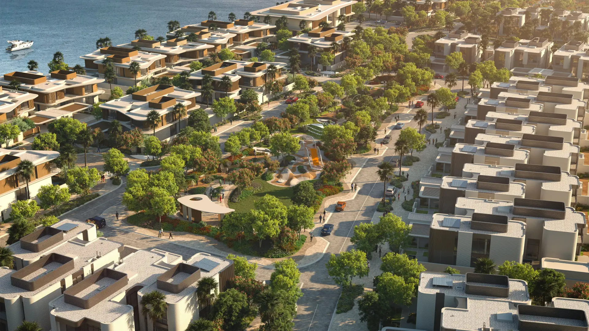 Aerial view of Yas Riva, showing rows of waterfront and inland townhouses with a central landscaped park featuring a children's playground, tree-lined streets, and boats moored along the shoreline.